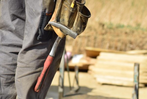 Bouwvakker met gereedschapsgordel tijdens renovaties beoordelen op een zonnige bouwplaats