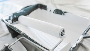 Verfroller in een bak met witte verf voor offertes voor schilderwerk