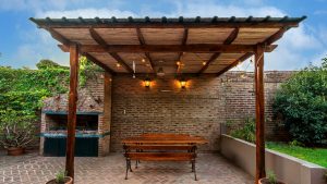 Beschutte zitplek met houten overkapping, tuinbank en sfeerverlichting voor gezellige avonden.